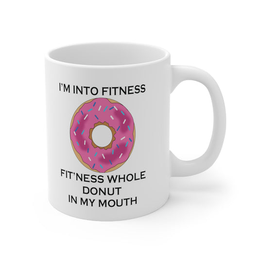 A white ceramic coffee mug with a design of a donut with pink icing and a funny quote: I'm Into Fitness, Fitness Whole Donut In My Mouth