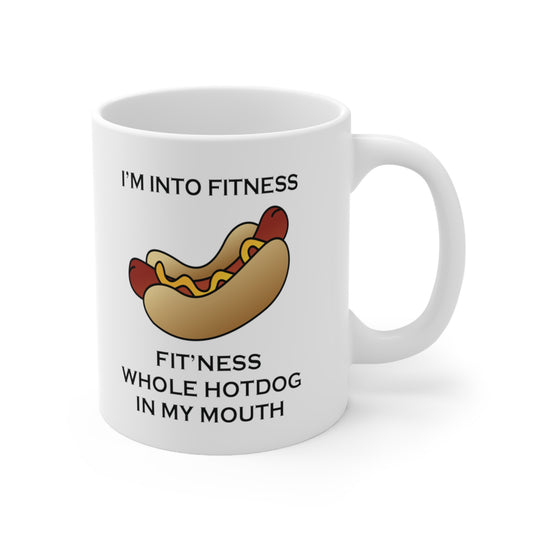 A white ceramic coffee mug with a design of a hotdog and a funny quote: I'm Into Fitness, fit'ness Whole hotdog In My Mouth
