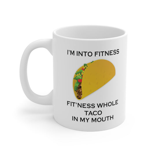 A white ceramic coffee mug with a design of a taco and the funny quote: I'm Into Fitness, Fit'ness Whole Taco In My Mouth