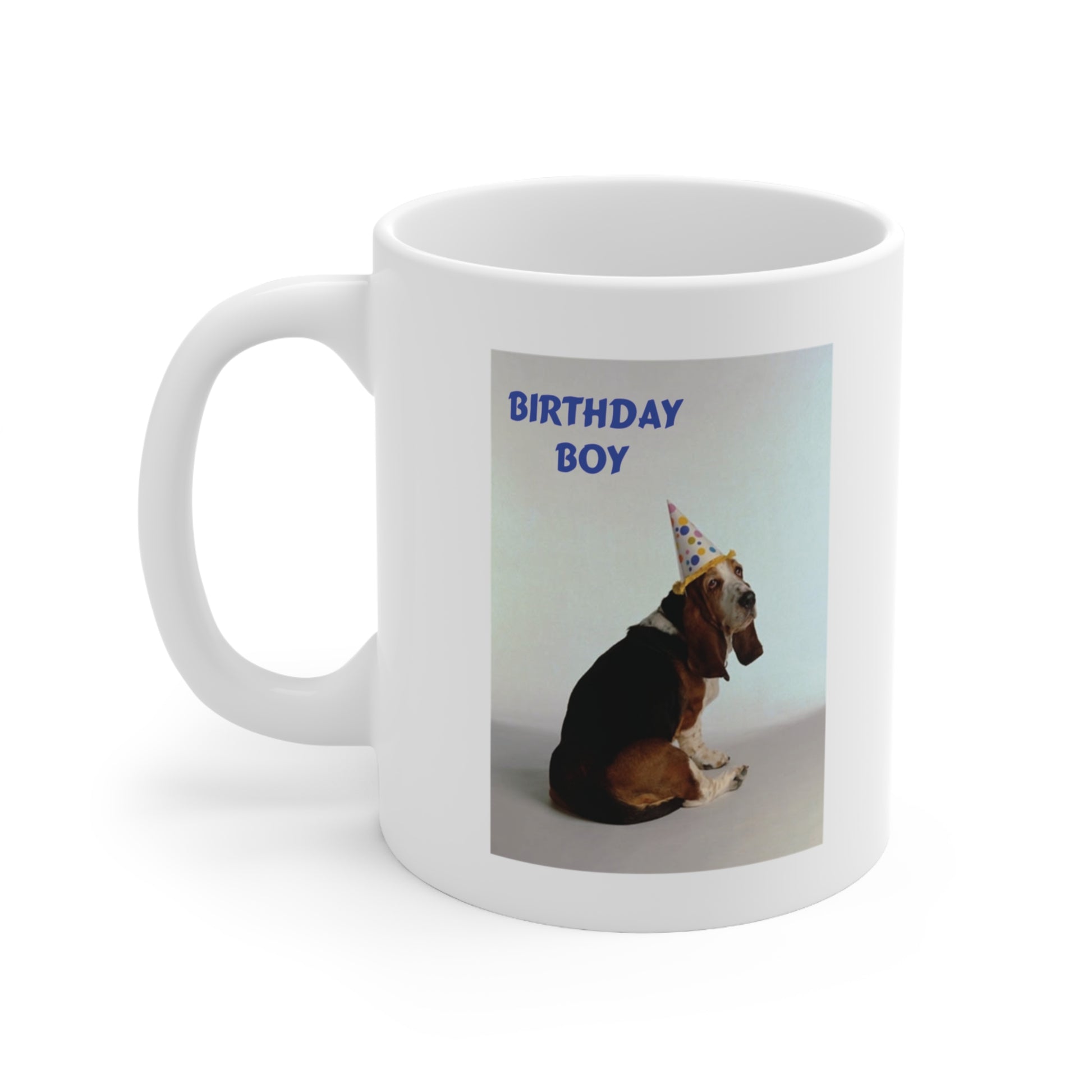 A white ceramic coffee mug with a photo of a Basset dog wearing a party hat. The quote reads: Birthday Boy