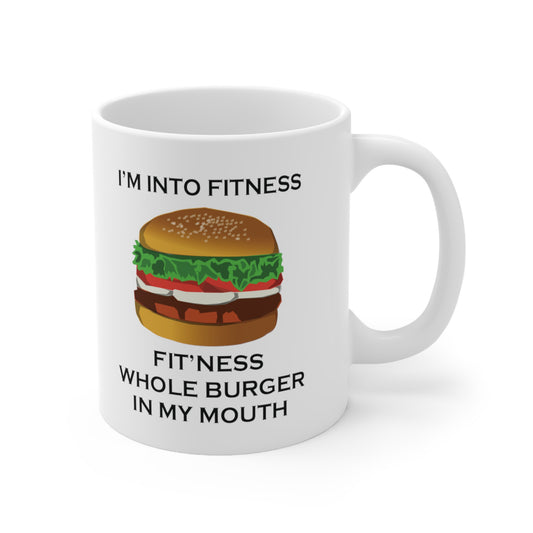 A white ceramic coffee mug with a design of a burger and the funny quote: I'm Into Fitness, Fit'ness Whole Burger In My Mouth