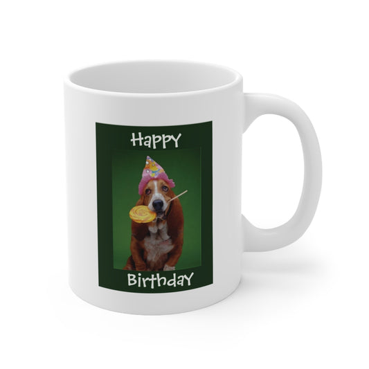 A white ceramic coffee mug with a photo of a Basset hound dog wearing a party hat, with a yellow lollipop in her mouth. The quote reads: Happy Birthday