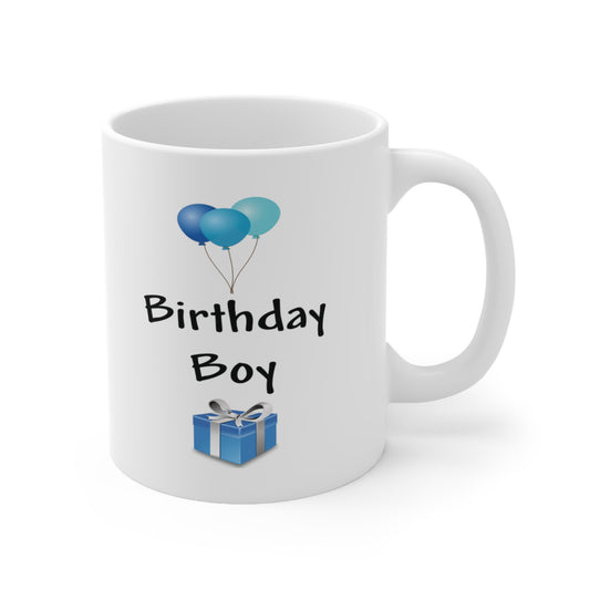 A white ceramic coffee mug with a design of blue balloons and a blue birthday present. The words read: Birthday Boy